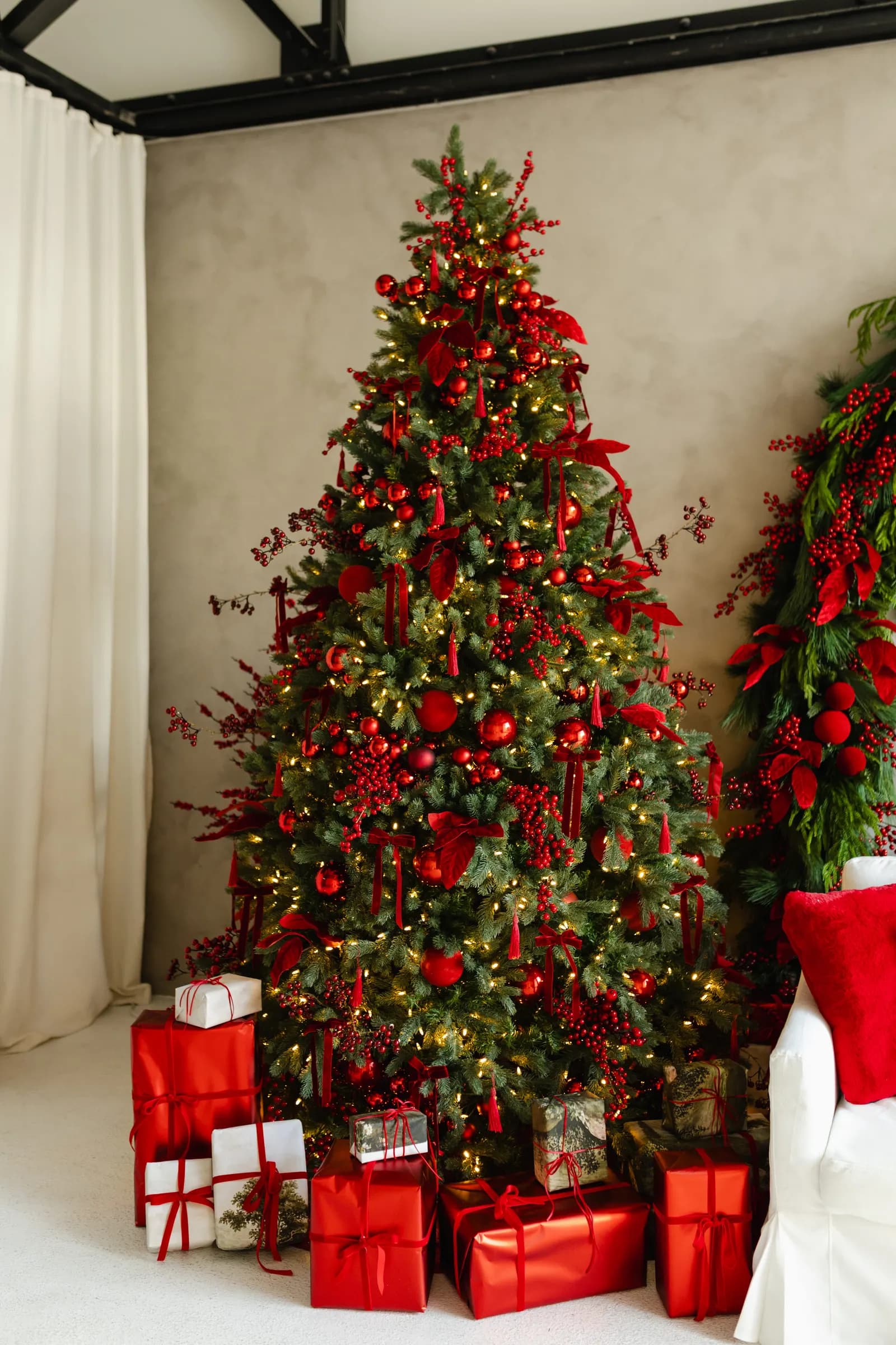 The Christmas tree on the Bordeaux Berry set, hung with red ornaments, berries and warm lights, with wrapped gifts underneath