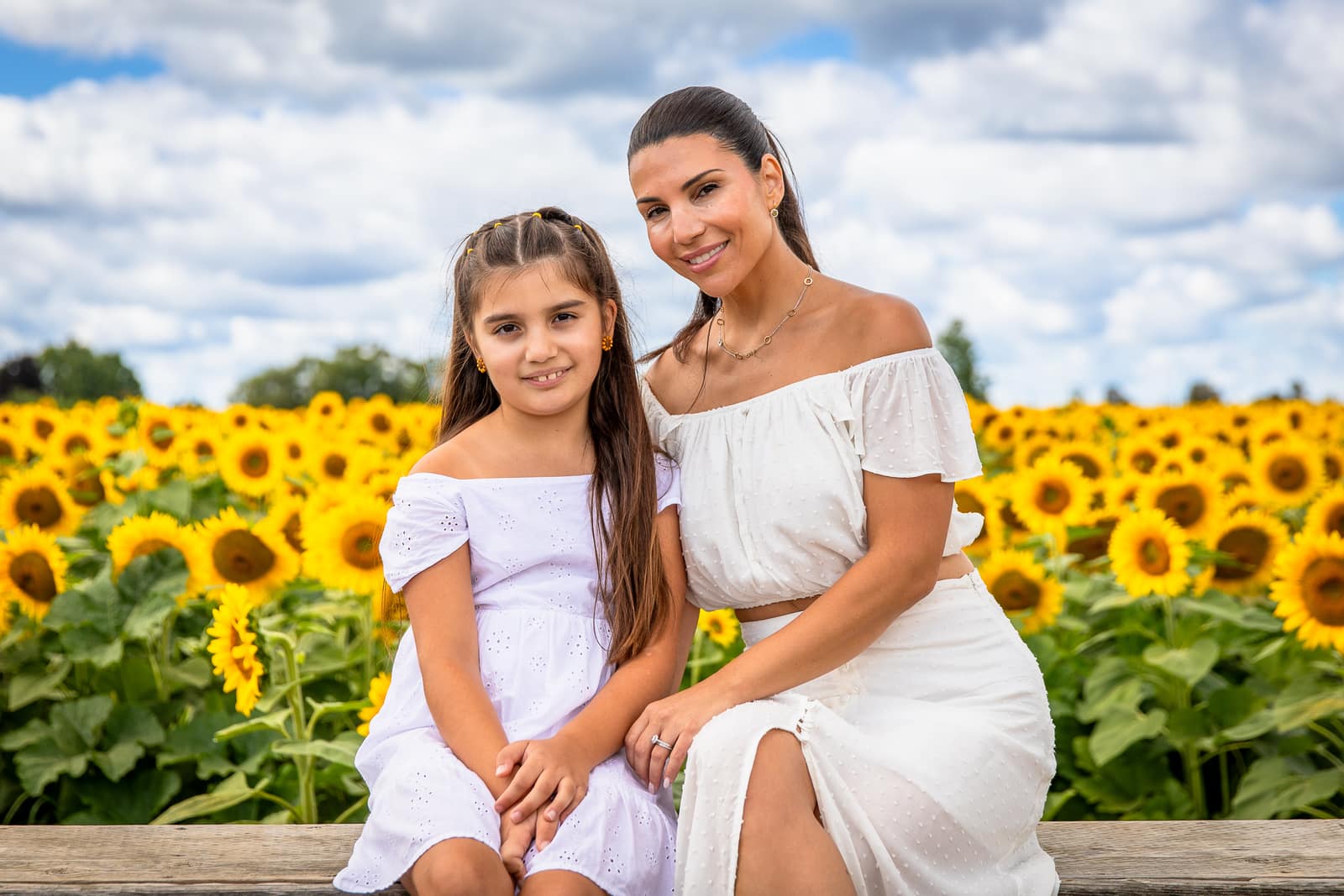 A mother and daughter on a bench in front of sunflowers
