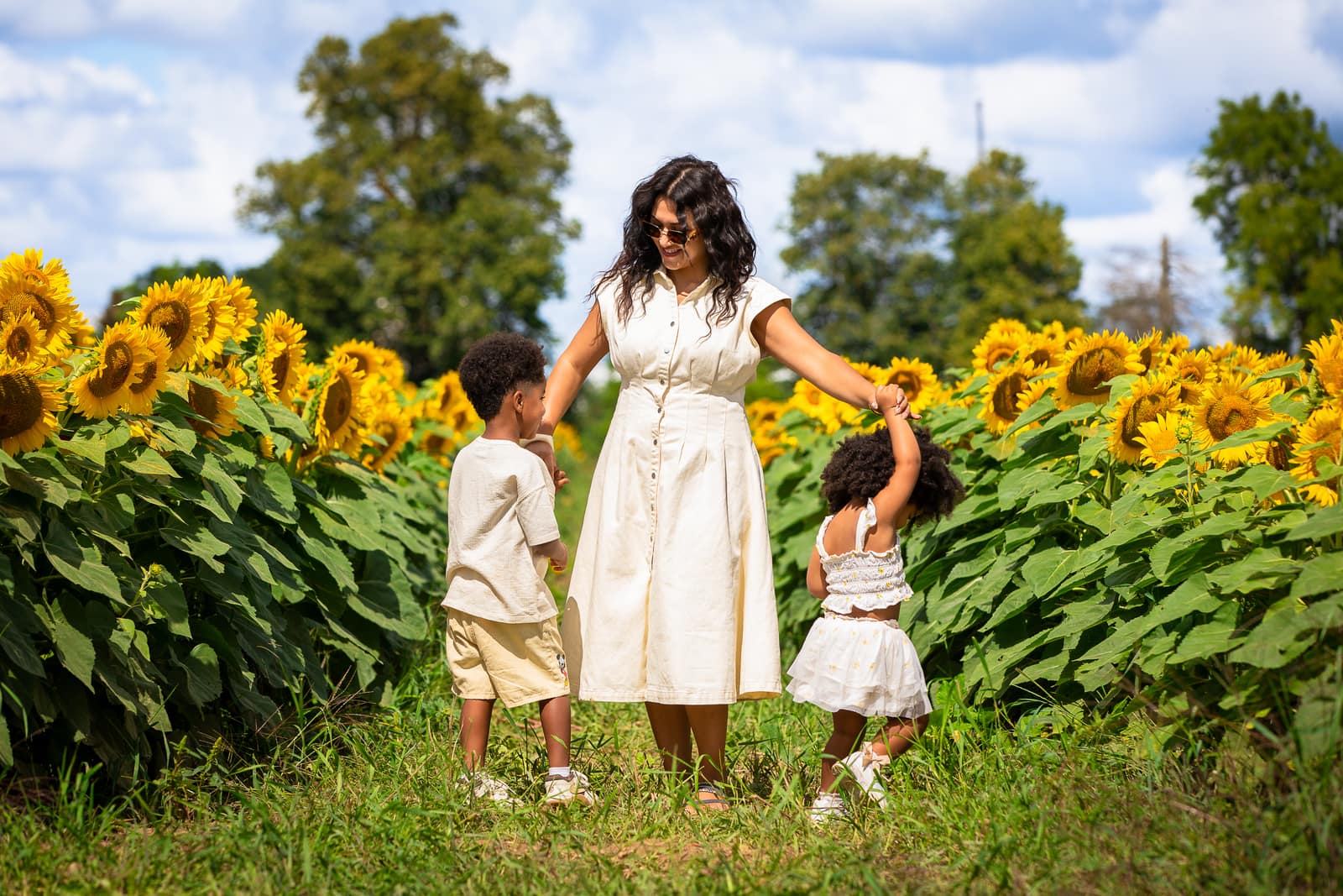 A mother swinging her daughter's arm beside her son in a sunflower field