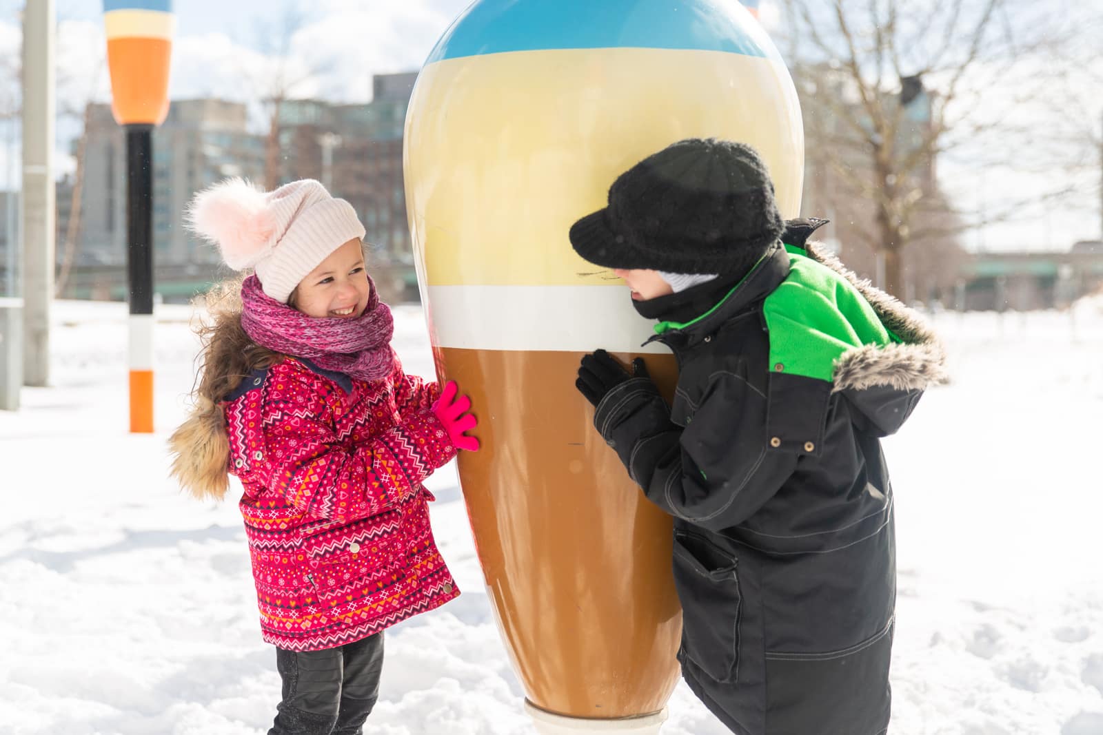 Two children in snowsuits either side of a sculpture in the snow