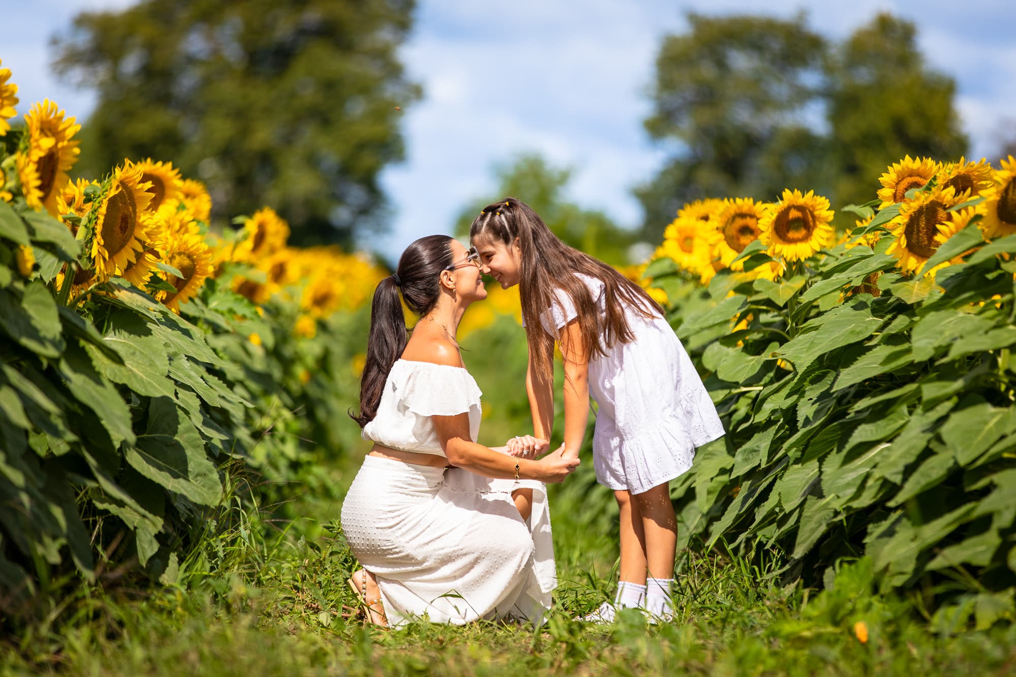 A mother kneeling in the field, nose to nose with her daughter