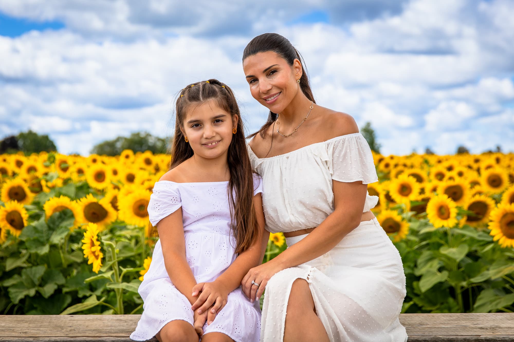 A mother and daughter sitting on a bench, the sunflowers behind them