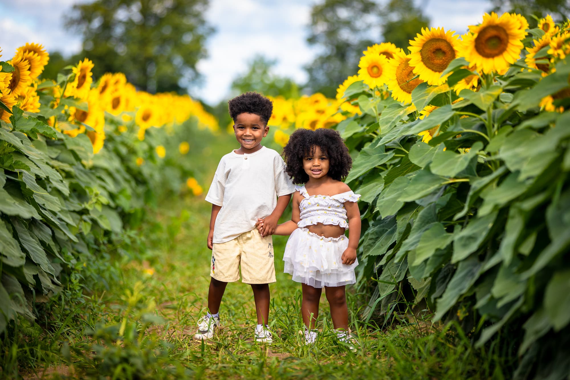 A brother and sister standing hand in hand in the row, smiling at the camera