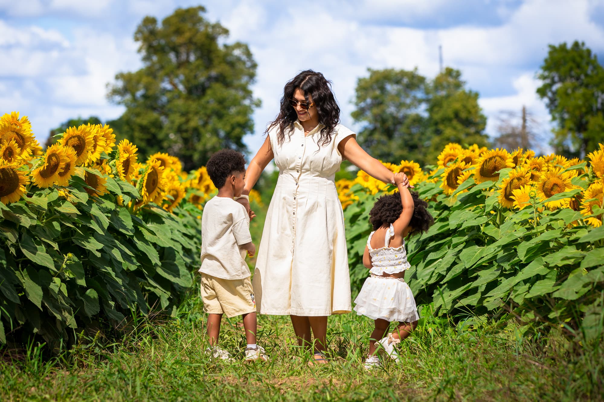 A mother walking through the field holding both her children's hands